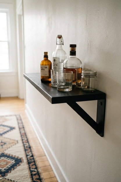 A wall mounted matte black floating shelf holding bar bottles