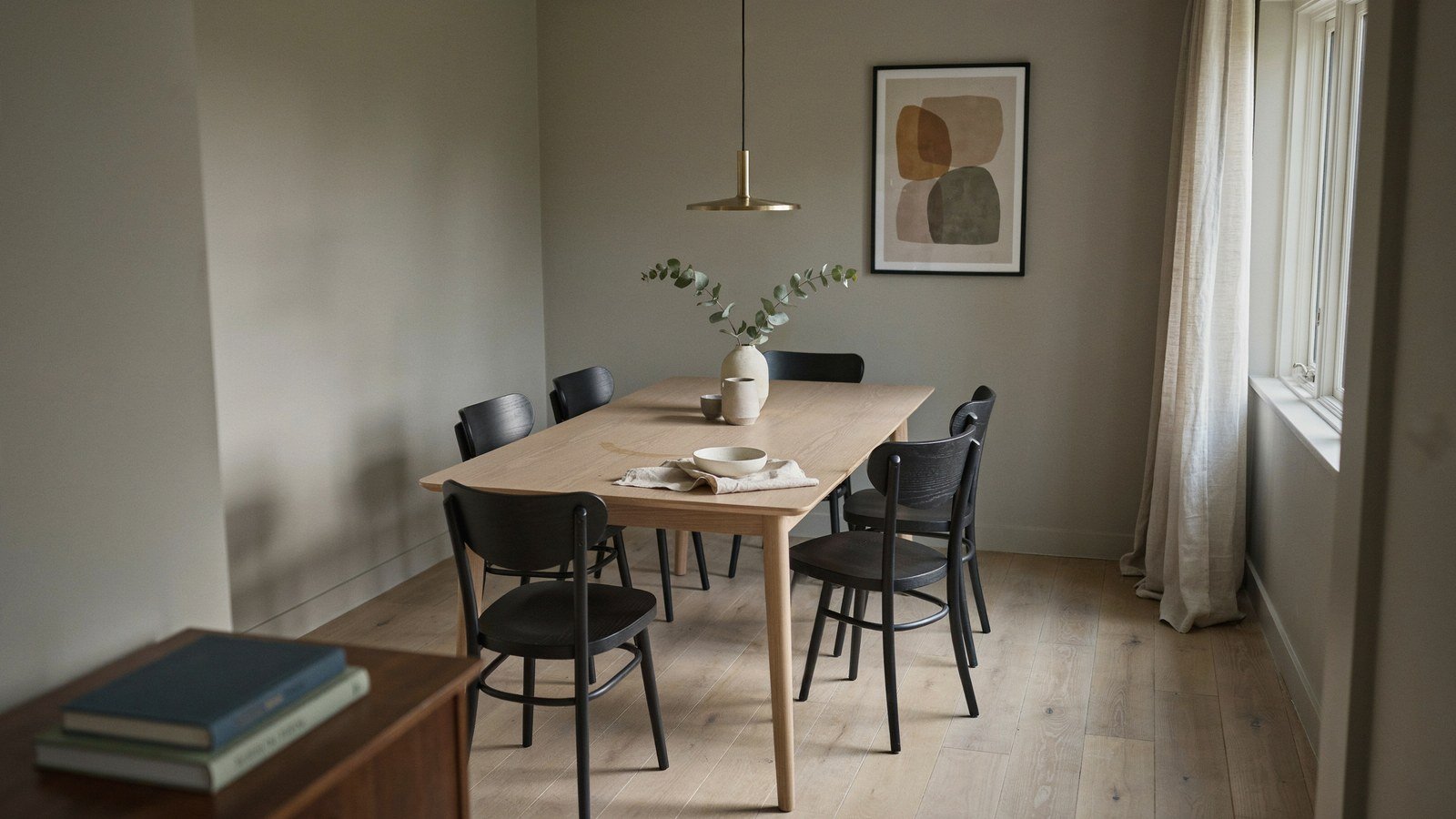 Pale dining table with dark chairs under a single low pendant