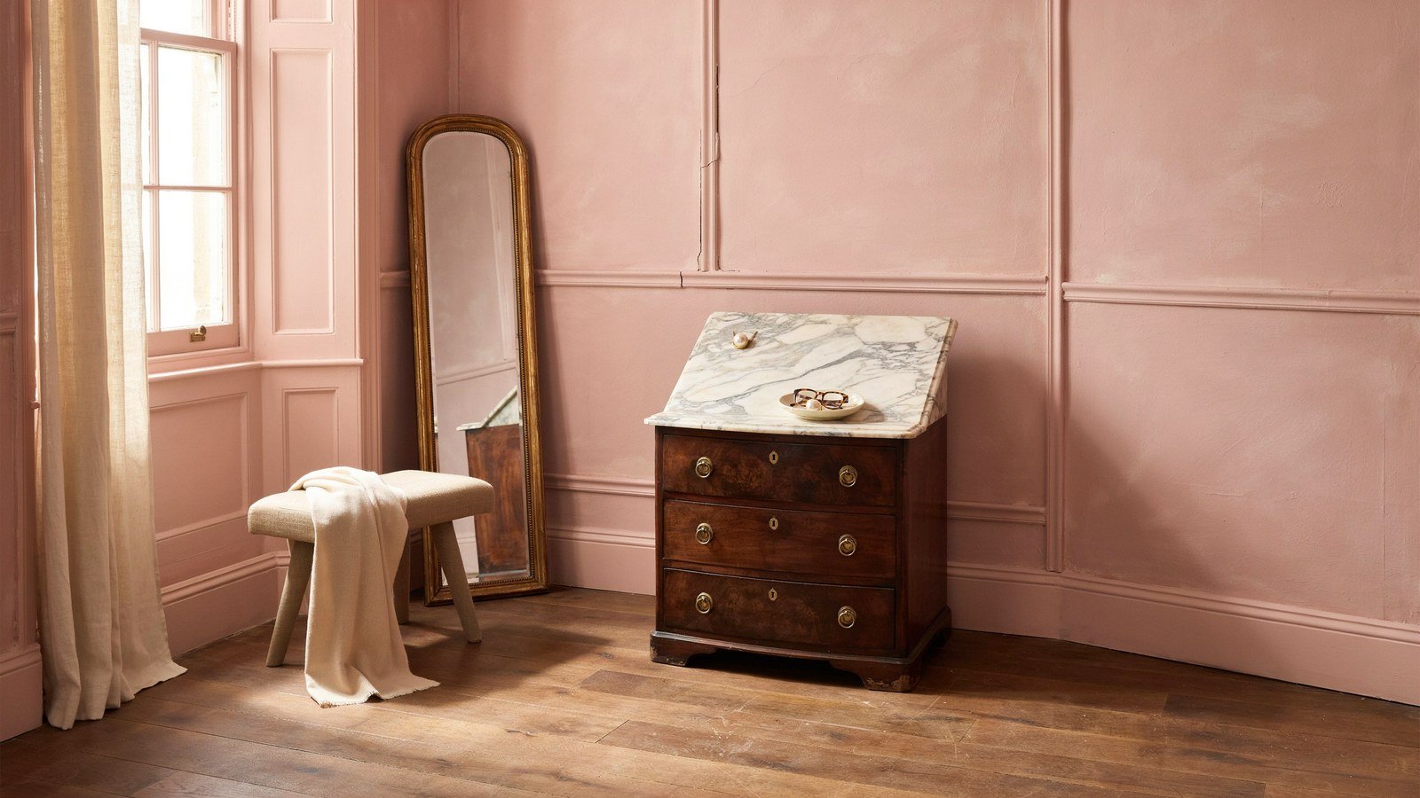 A romantic French dressing room with panelled walls, an antique chest and a leaning mirror
