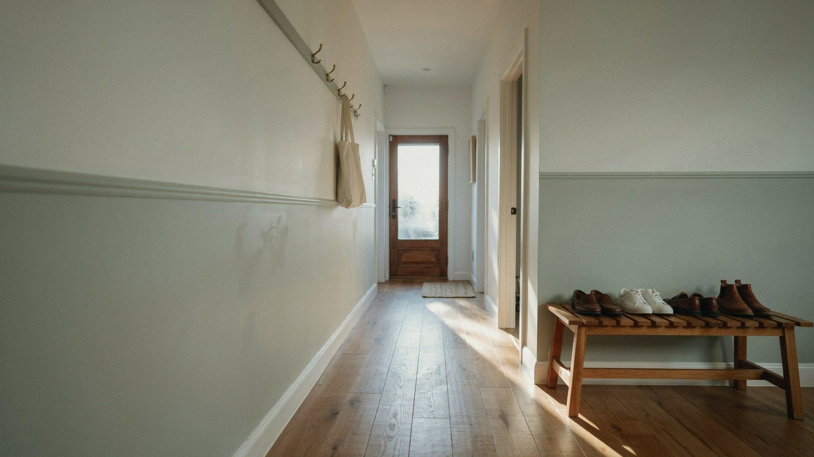 Small entryway with soft sage lower walls, an oak bench and brass hooks