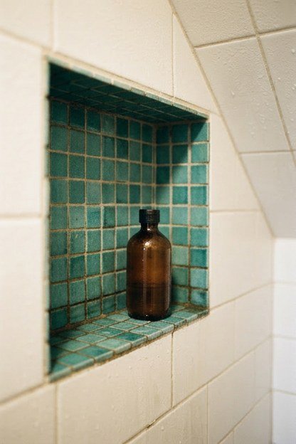 A recessed teal mosaic tile shower niche in an attic bathroom shower