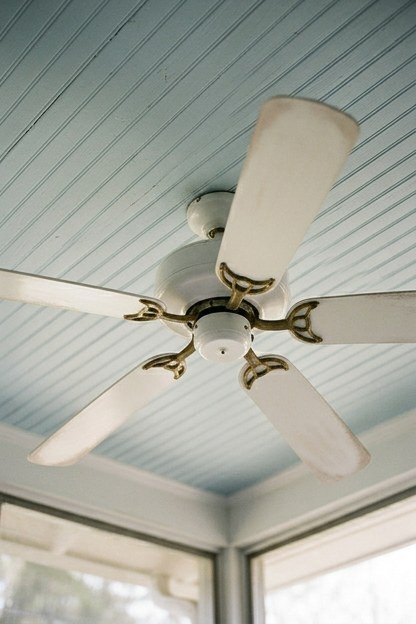 A white bladed ceiling fan mounted on a screened porch ceiling