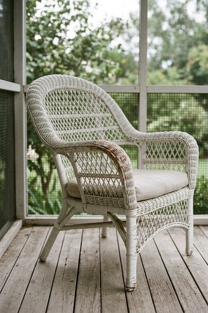 A white painted wicker chair with an open weave on a porch